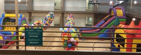 Obstacle course, giant slide, and bounce house inside community center gym